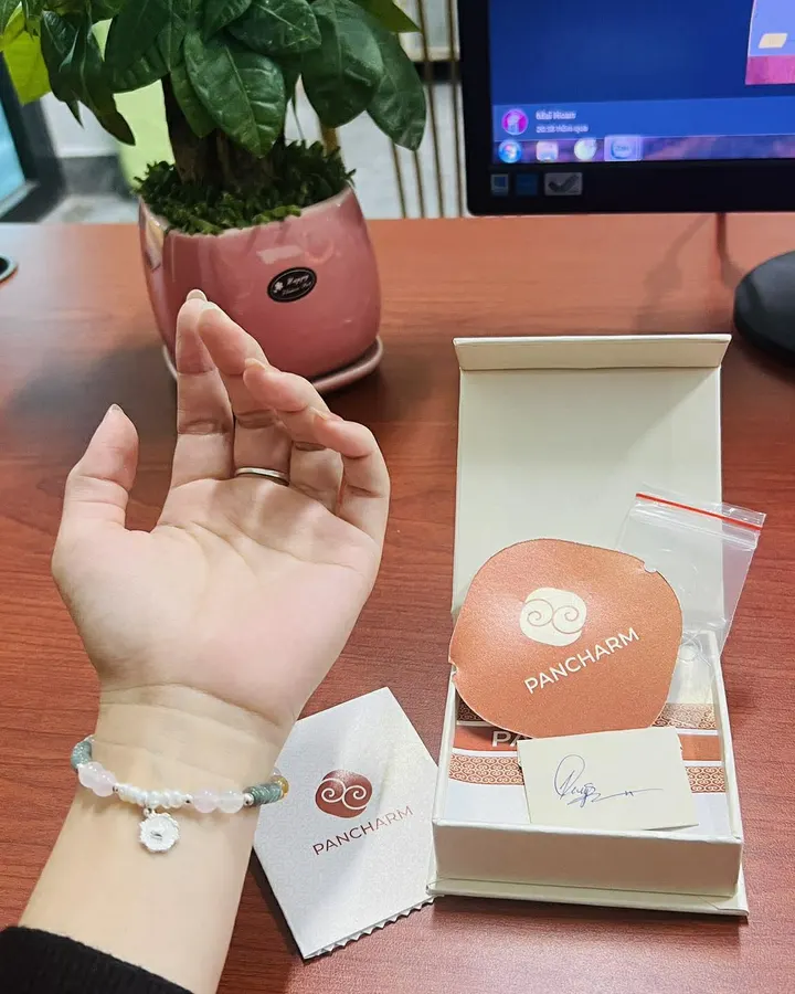 Ảnh khách gửi: cổ tay đeo vòng hạt trắng bên hộp quà Pancharm trên bàn làm việc