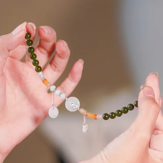 Hai bàn tay nâng chuỗi Thiên Ân dài: ngọc xanh đậm, đá cam, đồng điếu ngọc trắng và charm rơi